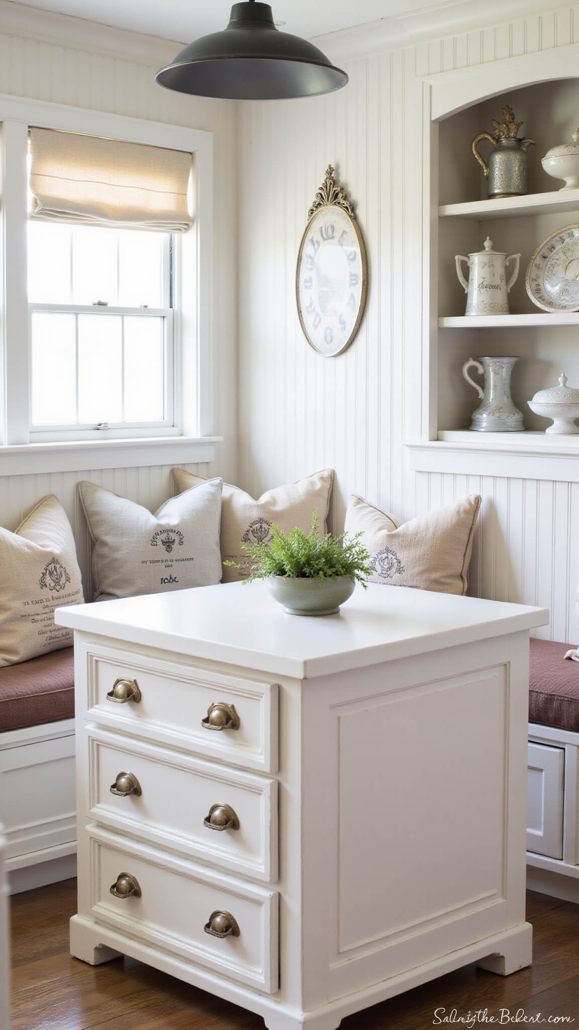 Cozy farmhouse breakfast nook with built-in banquette seating, aged brass cup pulls, vintage pillows, and soft morning light highlighting beadboard and antique mirror accents.