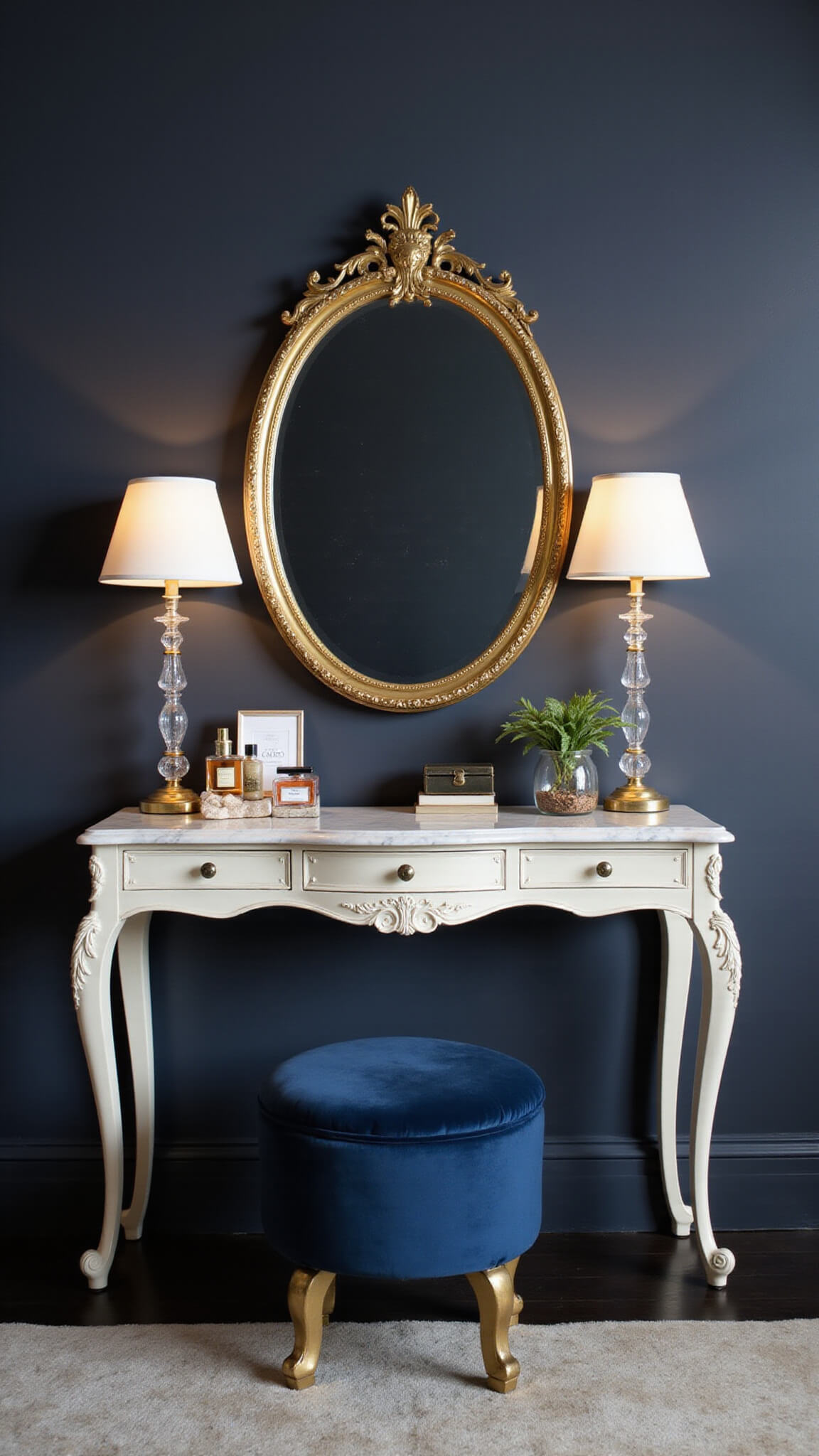 Luxury bedroom vanity with gold mirror, crystal lamps, navy velvet stool, and marble console against charcoal walls at blue hour.