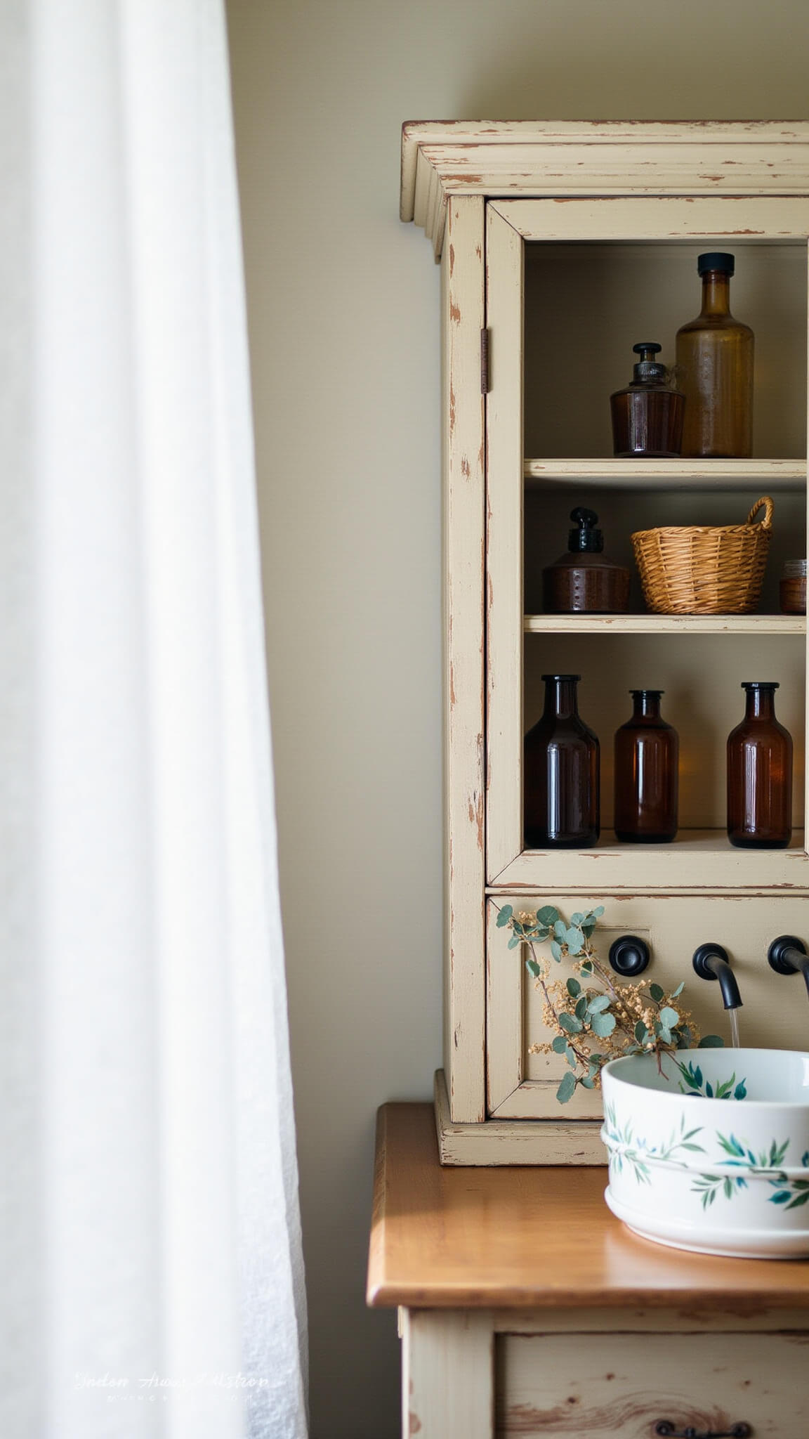 Vintage bathroom with morning light filtering through sheer curtain, showcasing amber glass bottles, woven baskets, botanical ceramic sink on reclaimed wood vanity, and dried pampas grass.