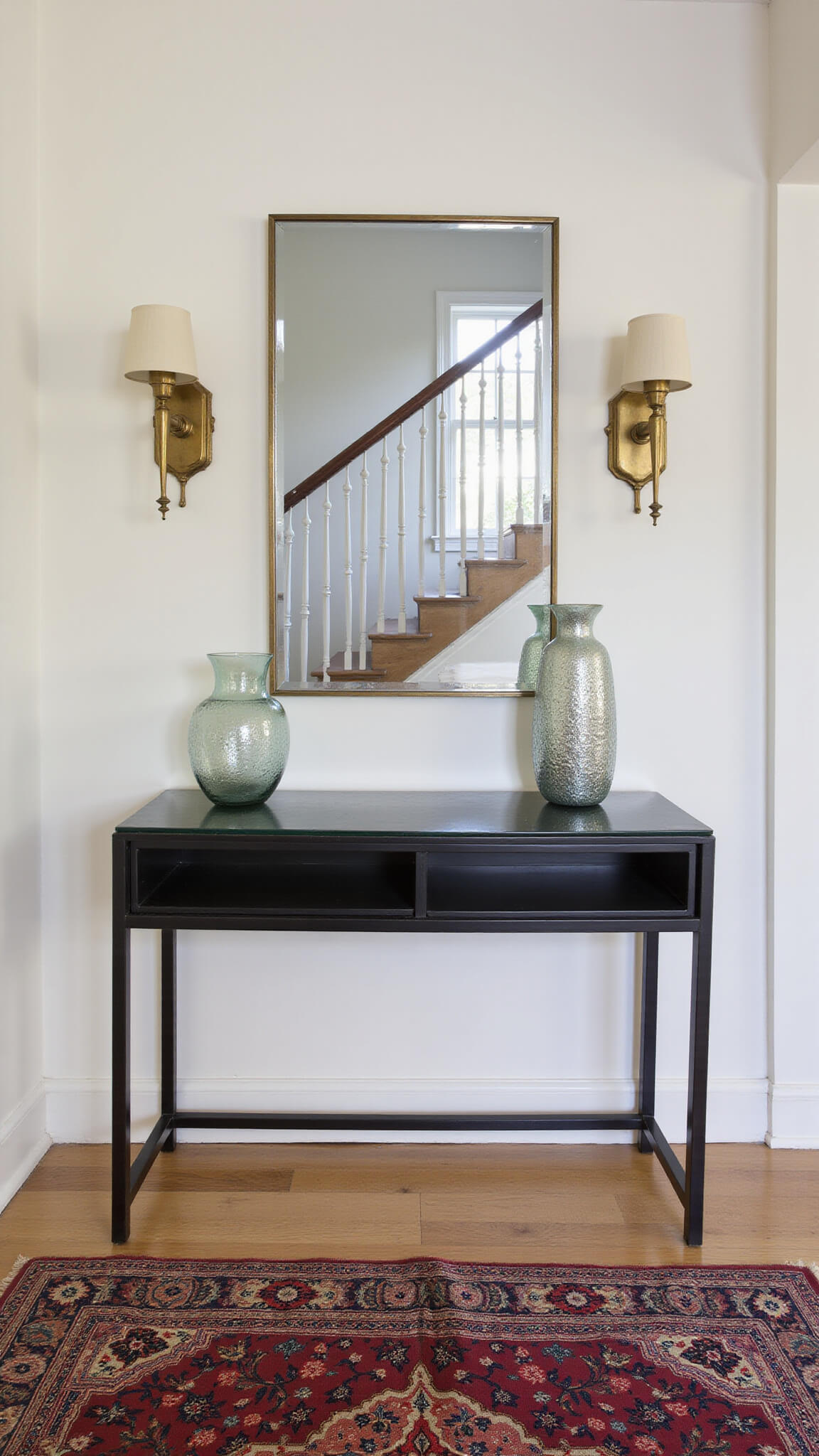 Dramatic top-down view of eclectic entryway with black steel console, mercury glass vessels, vintage runner, and modern staircase with restored bannister.