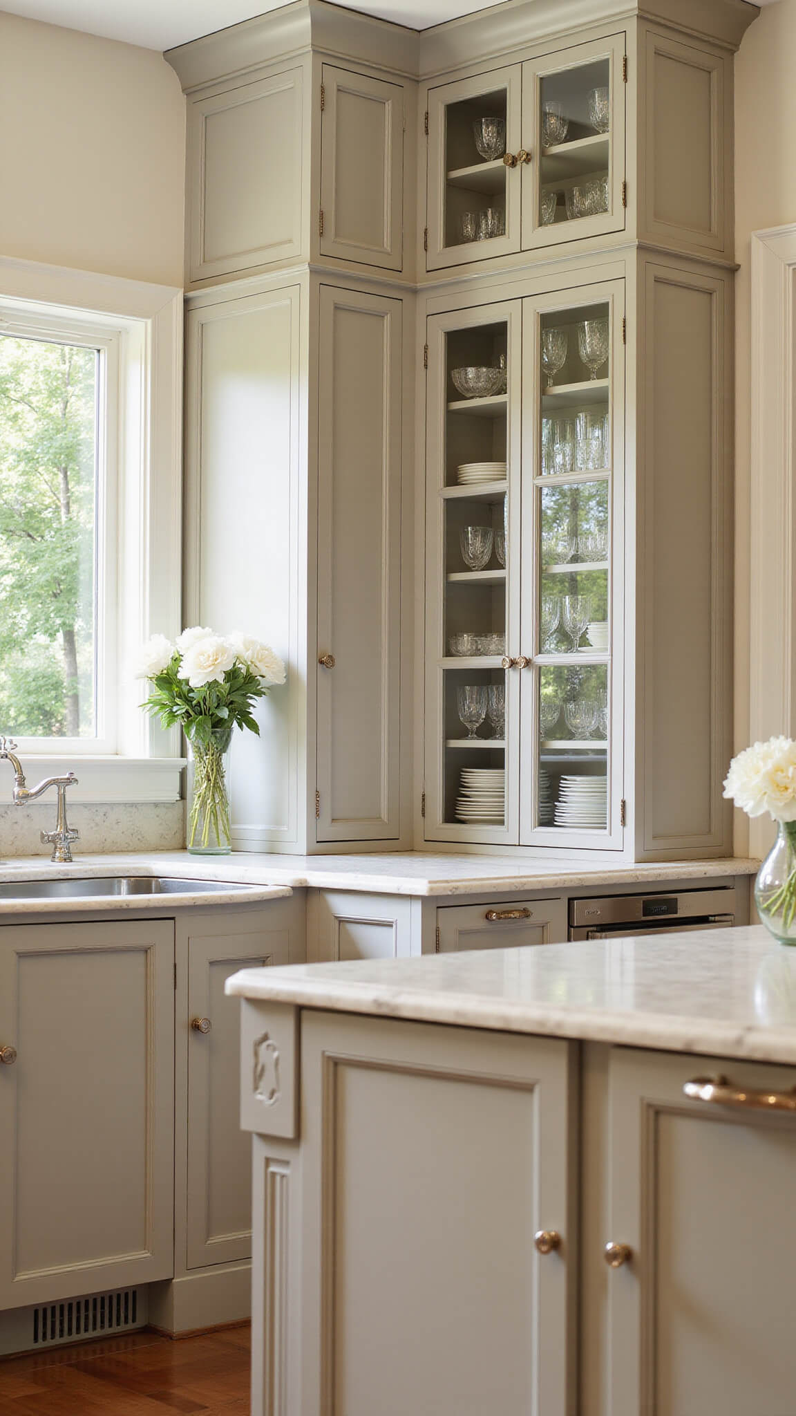 Transitional 20x15ft kitchen with greige cabinets, marble island, and natural light highlighting crystal glassware and silver accents.