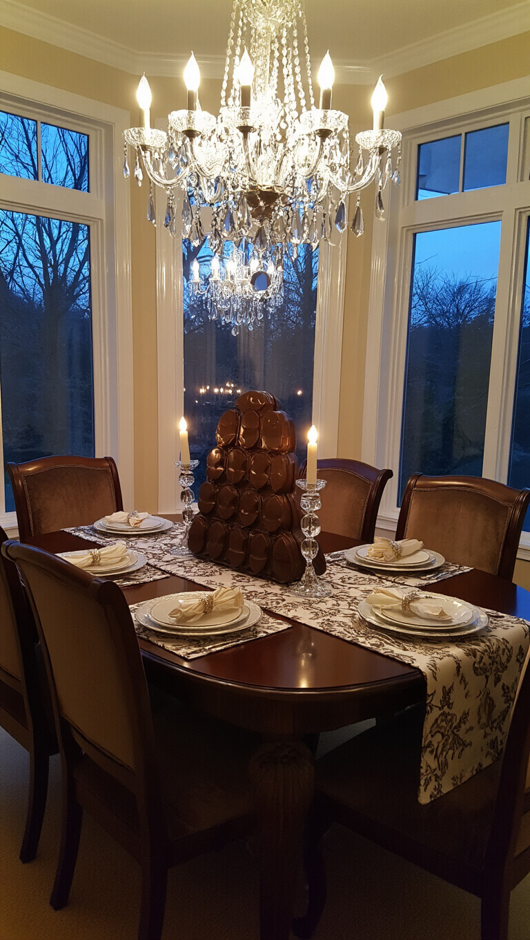 Elegant formal dining room at twilight with vintage chocolate mold centerpiece, mercury glass candlesticks, and crystal chandelier casting prismatic light over a damask-covered table with dark cherry furniture and velvet chairs.