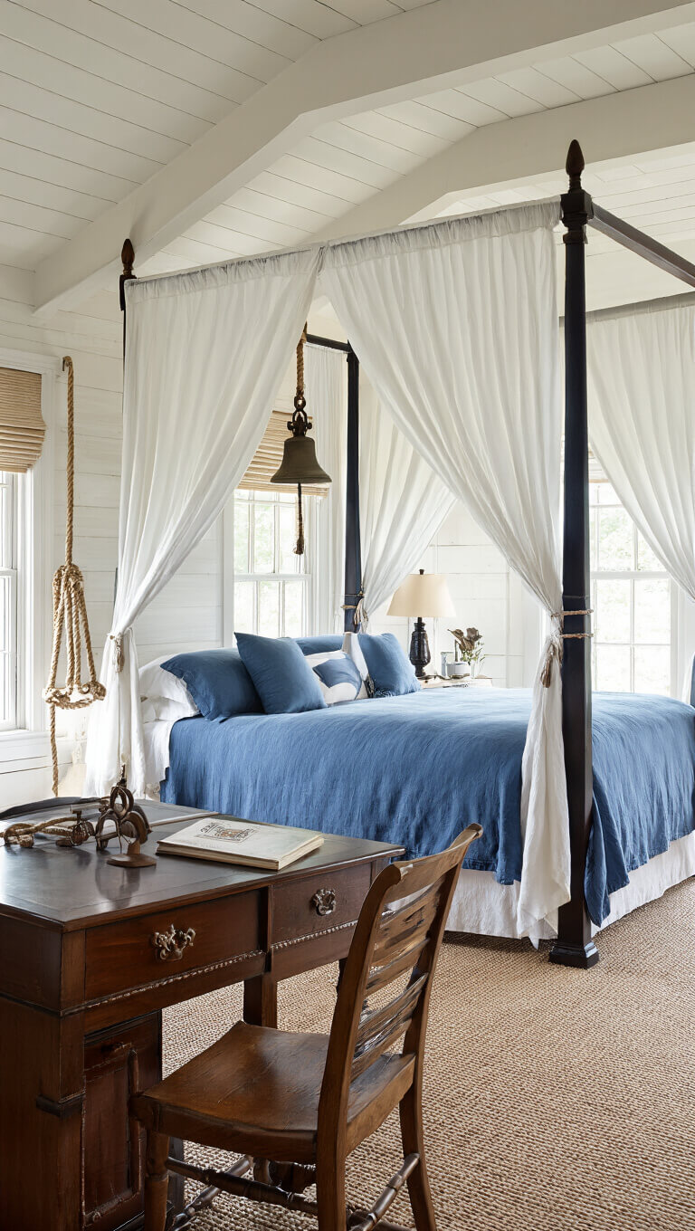 Traditional 13x15ft bedroom with maritime blue four-poster bed, white linen canopy, ship's bell bedside light, antique captain's desk, and hand-knotted rope art, seen from above in morning light.