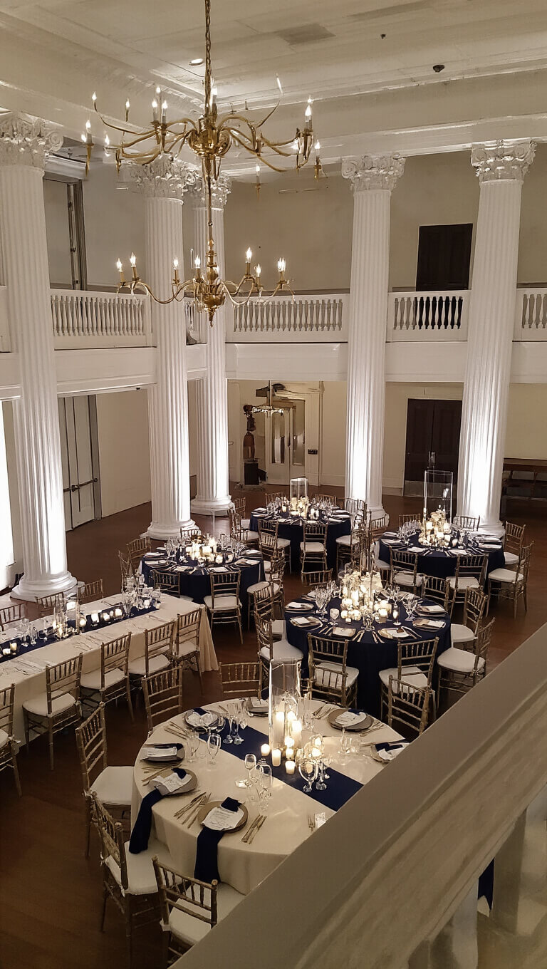 Wide-angle view of elegant ballroom reception with mixed table styles, crystal stemware, silk and velvet table decor, and modern brass chandeliers under dramatic evening lighting.