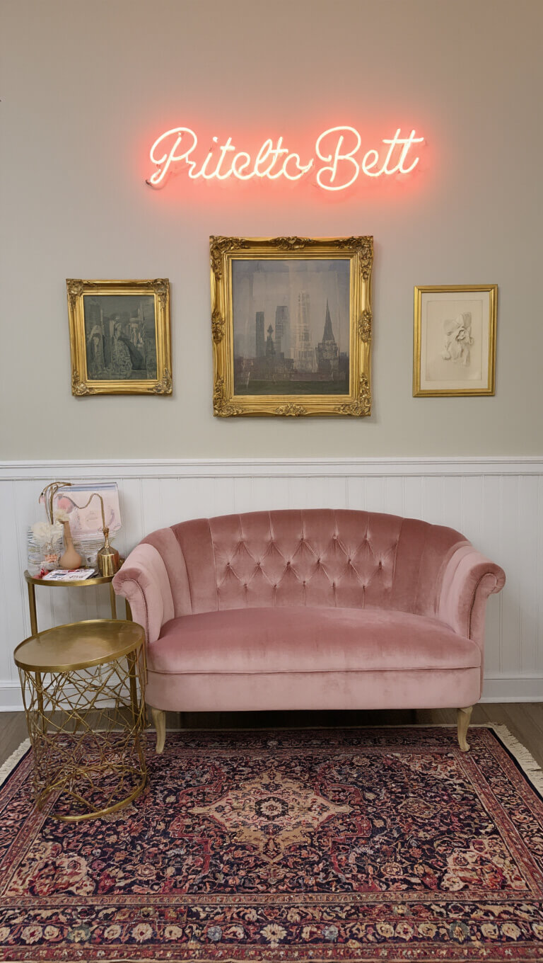 Charming 10x12ft photo booth with blush pink velvet settee, gold vintage frames, neon sign, Persian rug, and ambient evening lighting.