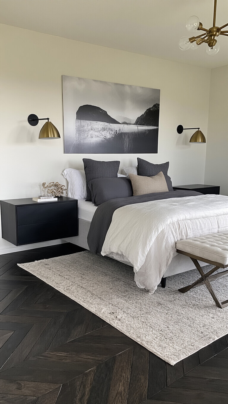 Dawn-lit 14x15ft bedroom with ebony chevron wood floors, statement bed with matte black floating nightstands, charcoal and ivory bedding, black-and-white abstract photography, and aged brass lighting.